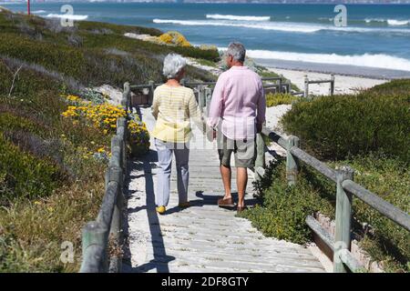 Älteres kaukasisches Paar, das die Stufen zum Strand hinunter läuft und Hände hält Stockfoto