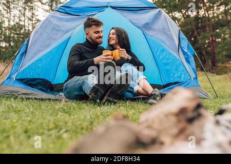 Ein paar fröhliche Touristen, die Tee trinken, während sie in der Nähe des Zeltes sitzen Stockfoto
