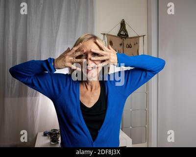 Ein flacher Fokus einer fröhlichen blonden Frau mittleren Alters Ihr Gesicht mit den Fingern Stockfoto