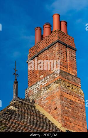 Traditionell gebaut roten Backstein Schornstein Stapel und Terrakotta-Kamin Töpfe auf einem viktorianischen Gebäude mit einem gusseisernen Blitzableiter Finial. Stockfoto