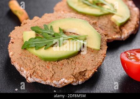 Leckeres frisches Sandwich mit Leberpaste, Avocado-Stücken und einer Rucola auf einem dunklen Betontisch Stockfoto