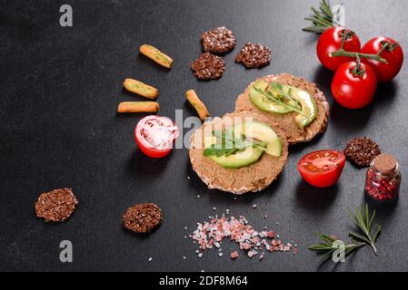 Leckeres frisches Sandwich mit Leberpaste, Avocado-Stücken und einer Rucola auf einem dunklen Betontisch Stockfoto