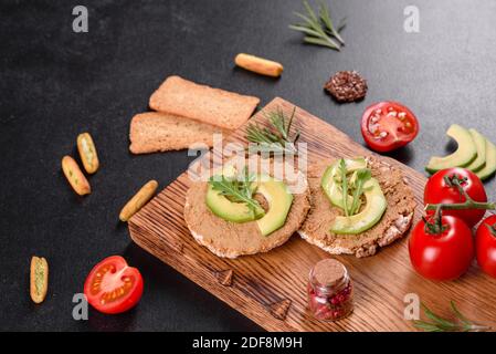 Leckeres frisches Sandwich mit Leberpaste, Avocado-Stücken und einer Rucola auf einem dunklen Betontisch Stockfoto