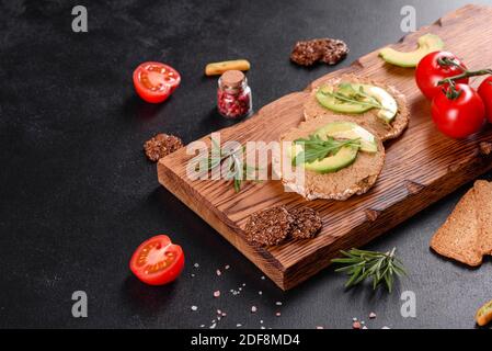 Leckeres frisches Sandwich mit Leberpaste, Avocado-Stücken und einer Rucola auf einem dunklen Betontisch Stockfoto