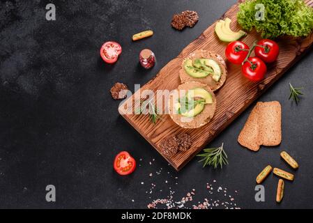 Leckeres frisches Sandwich mit Leberpaste, Avocado-Stücken und einer Rucola auf einem dunklen Betontisch Stockfoto