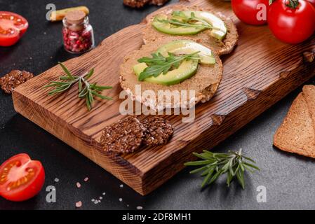 Leckeres frisches Sandwich mit Leberpaste, Avocado-Stücken und einer Rucola auf einem dunklen Betontisch Stockfoto