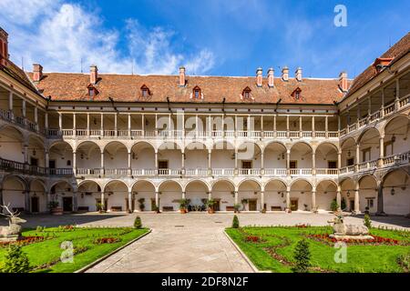 Opocno, Tschechische Republik - Juni 16 2020: Blick auf den Schlosshof mit Arkaden und roter Fassade. Grüner Rasen mit Hirsch-Statuen und Blumen im Vorgarten Stockfoto