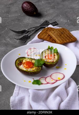 Keto Diätgericht: Gebackene Avocado Boote mit Eiern auf weißem Teller, Rettich und Toast. Nahaufnahme Stockfoto