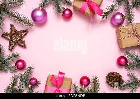 Weihnachtsrahmen aus Tannenzweigen, Weihnachtsschmuck und Geschenkschachteln auf pastellrosa Hintergrund. Stockfoto