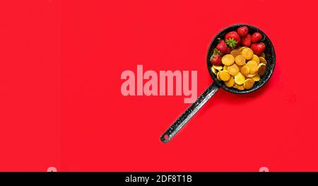 Trendiges Essen - Pfannkuchen Müsli. Mini-Cerealien-Pfannkuchen mit Erdbeeren in einer Pfanne auf rotem Hintergrund, Platz zum Kopieren Stockfoto