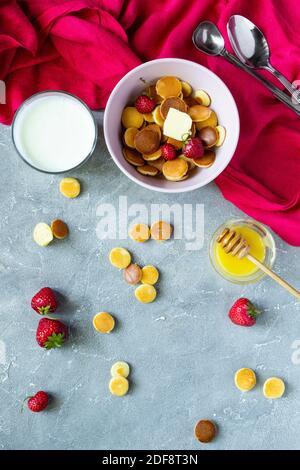 Trendiges Essen - Pfannkuchen Müsli. Mini-Cerealien-Pfannkuchen mit Erdbeeren in einer Pfanne auf rotem Hintergrund, Platz zum Kopieren Stockfoto