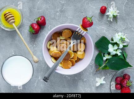 Trendiges Essen - Pfannkuchen Müsli. Haufen Mini-Cerealien-Pfannkuchen mit Erdbeeren. Ansicht von oben oder flach liegend. Stockfoto