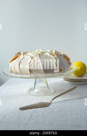 Hausgemachte Baiser Pavlova mit Schlagsahne und Zitrone auf Glaskuchenständer auf dem hellen Hintergrund Stockfoto