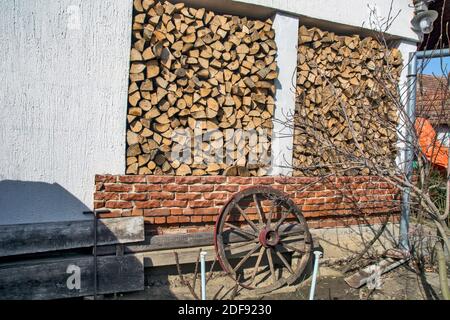 Brennholz wird im Haushalt gelagert, wenn der Winter eintrifft. Ein Rad aus alten Dorfwagen lehnt sich an die Wand. Stockfoto