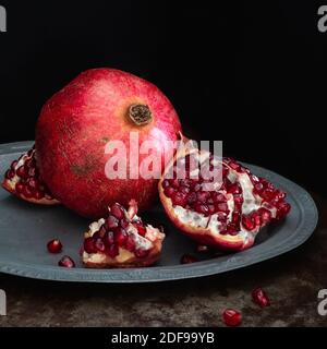 Granatapfel Obst ganz und öffnen auf einer silbernen Platte und schwarzem Hintergrund, quadratisch Stockfoto