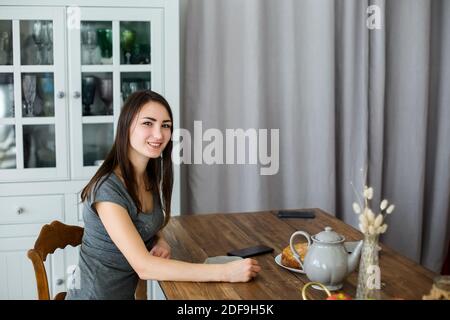 Brunette Mädchen sitzt in der Küche an einem Holztisch, ein Wasserkocher mit Tee Stockfoto