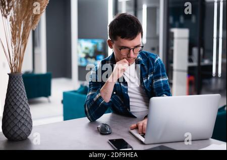 Porträt eines nachdenklichen jungen Geschäftsmannes, der von zu Hause aus mit einem Laptop arbeitet. Stockfoto