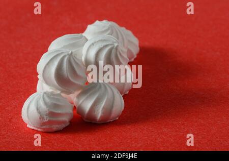 Mehrere Meringues in einer Pyramide auf einem strukturierten roten Hintergrund gestapelt. Selektiver Fokus. Stockfoto