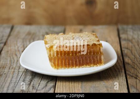 Honig in Wabe auf einem weißen Teller auf einem rauen Holzhintergrund. Selektiver Fokus. Stockfoto