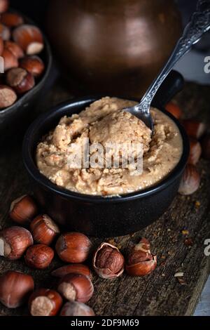 Haselnussbutter in Keramikbecher mit geschälten Haselnüssen auf Holzgrund. Stockfoto