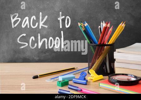 Back to School auf Tafel mit mehreren Schreibwaren auf Holztisch geschrieben. Stockfoto