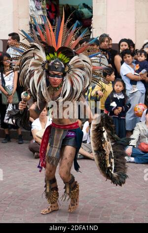 Eine AZTEKISCHE TÄNZERIN, die als KRIEGER mit Kopfschmuck, Rassel und Schild während des CERVANTINO FESTIVALS - GUANAJATO, MEXIKO, gekleidet ist Stockfoto