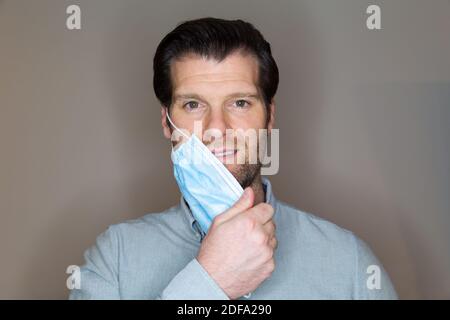 Hübscher junger Kaukasusmann, der eine Gesichtsmaske auszieht, nachdem er vom Coronavirus geheilt wurde. Stockfoto