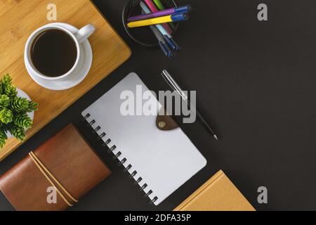 Notizblock, Stift und Kaffee auf schwarzem Hintergrund. Bürotisch Stillleben. Stockfoto