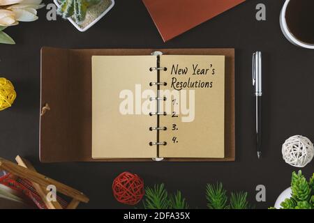 Neujahrsvorsätze Text auf rustikalem Notizblock mit Stift und Kaffee auf schwarzem Hintergrund. Stockfoto
