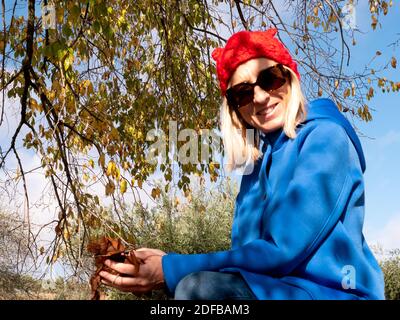 Ein flacher Fokus einer fröhlichen blonden Frau mittleren Alters, die hält Die gefallenen Blätter in ihren Händen Stockfoto