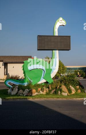 Vernal, Utah - 20. September 2020: Kitschiger grüner Dinosaurier am Straßenrand mit einem leeren Schild in der Innenstadt Stockfoto