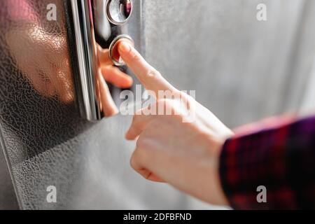 Der Daumen drückt die Elevator-Taste, eine Hand, die nach der Taste greift, das Mädchen wartet auf Elevator, Drucktaste Start, isoliert Stockfoto