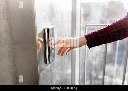 Der Daumen drückt die Elevator-Taste, eine Hand, die nach der Taste greift, das Mädchen wartet auf Elevator, Drucktaste Start, isoliert Stockfoto