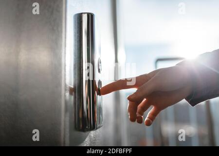 Der Daumen drückt die Elevator-Taste, eine Hand, die nach der Taste greift, das Mädchen wartet auf Elevator, Drucktaste Start, isoliert Stockfoto