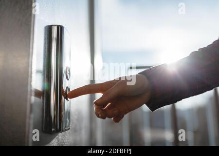 Der Daumen drückt die Elevator-Taste, eine Hand, die nach der Taste greift, das Mädchen wartet auf Elevator, Drucktaste Start, isoliert Stockfoto