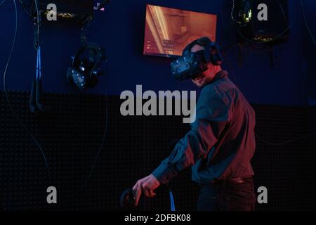 Zeitgenössischer Mann in Virtual Reality-Headset mit Joystick, während im dunklen Raum vr spielen Club und Videospiel. Stockfoto