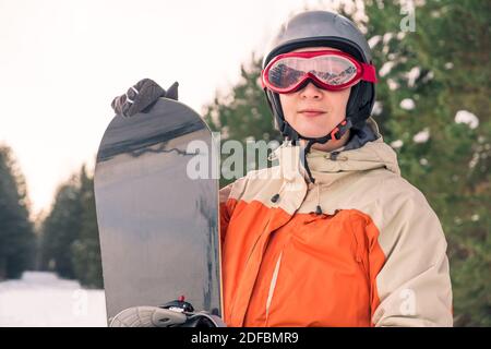Portrait einer Snowboarderin mit Helm und Brille vor Wald und Hang. Stockfoto