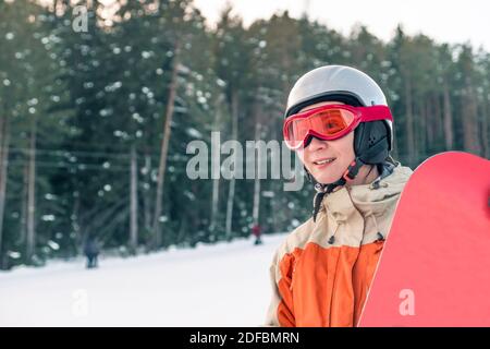 Portrait einer Snowboarderin mit Helm und Brille vor Wald und Hang. Stockfoto