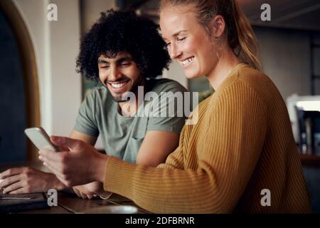 Schöne Frau und schöner Mann beim Video in Smartphone und Lachend im Café Stockfoto