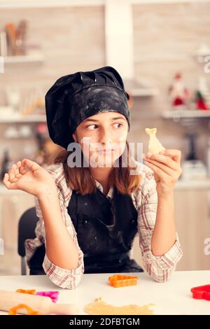 Enkelkind am weihnachtstag mit Blick auf geformte Pasterie trägt Schürze und bonette. Happy fröhlich freudig Teenager-Mädchen hilft älteren Frau Vorbereitung süße Kekse, um Winterferien zu feiern. Stockfoto