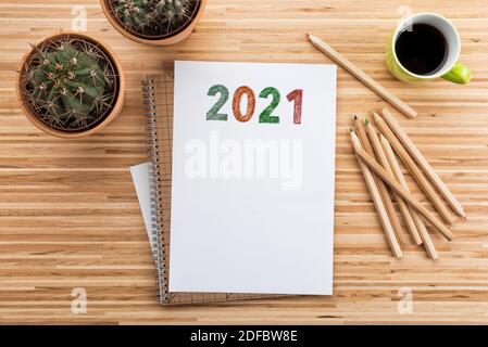 Jahr 2021 gezeichnet auf Papier auf Schreibtisch mit Kaffeetasse, Kaktuspflanzen, Notizblock und Farbstiften Stockfoto