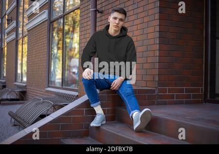 Mockup eines schwarzen Kapuzenpulloons auf einem jungen Kerl, Vorderansicht, Präsentation auf der Straße. Eine Vorlage für modische Kleidung für die Werbung im Online-Shop Stockfoto