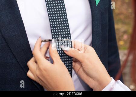 Die Braut setzt eine Klemme auf die Krawatte des Bräutigams. Bräutigam Gebühren am Hochzeitstag, Traditionen der Vorbereitung und Organisation. Stockfoto