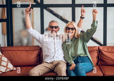 Reifes Paar in Sonnenbrille sitzt auf dem Sofa und Gefühl Freudig Stockfoto