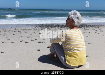 Ältere kaukasische Frau, die am Strand am Meer sitzt Stockfoto