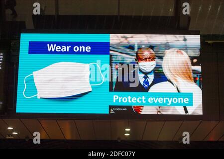 Glasgow, Schottland, Großbritannien. Dezember 2020. Im Bild: Sicherheitshinweis für öffentliche Informationen auf einem großen Fernsehbildschirm in der Queen Street Station in Glasgow, in dem Passagiere darauf hingewiesen werden, tragen SIE EINEN. SCHÜTZEN SIE ALLE. Auf dem Bildschirm wird eine Grafik einer Gesichtsmaske angezeigt. Quelle: Colin Fisher/Alamy Live News Stockfoto