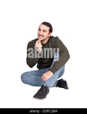 Nachdenklicher Casual Mann auf dem Boden sitzend lächelt zur Seite schauen, hält die Hand unter dem Kinn, nachdenkliche Geste. Lifestyle voller Länge Porträt glücklich Student Stockfoto