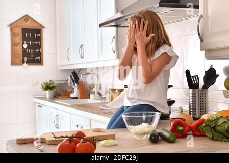 Kleines Mädchen auf Küchenbank sitzen und Essen mit Händen zubereiten Auf dem Gesicht zu Hause Stockfoto