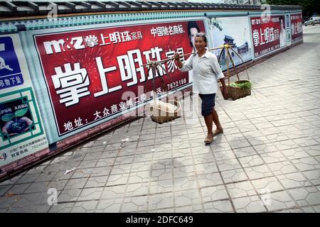 China, Verkäuferin, die zwei Körbe in einer Straße in Jianshui trägt Stockfoto