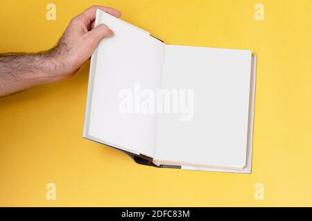 Männliche Hand öffnete ein Buch-Katalog auf gelbem Hintergrund, Modell-Serie Vorlage bereit für Ihr Design, Seitenauswahl Pfad enthalten. Stockfoto